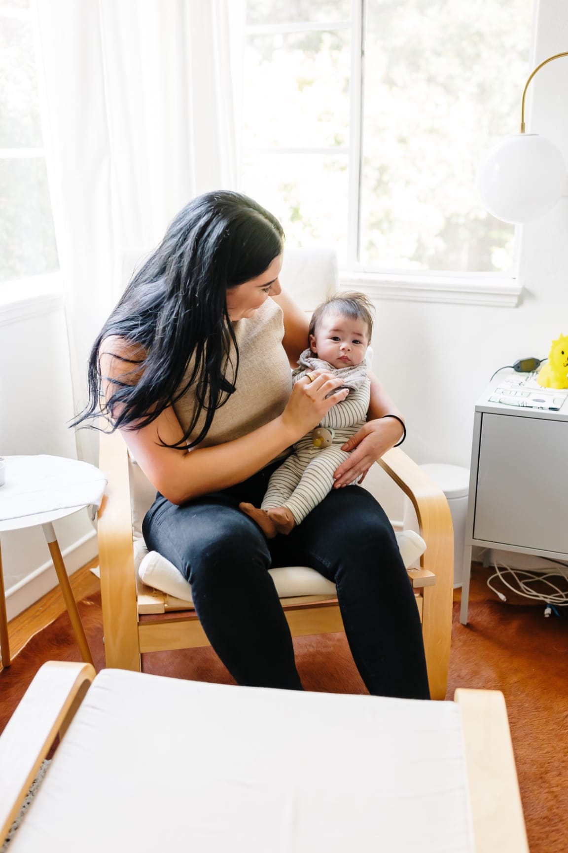 Ashlee McKenzie seated in a sunlit nursery, gently cradling a newborn in a soft moment of attuned presence